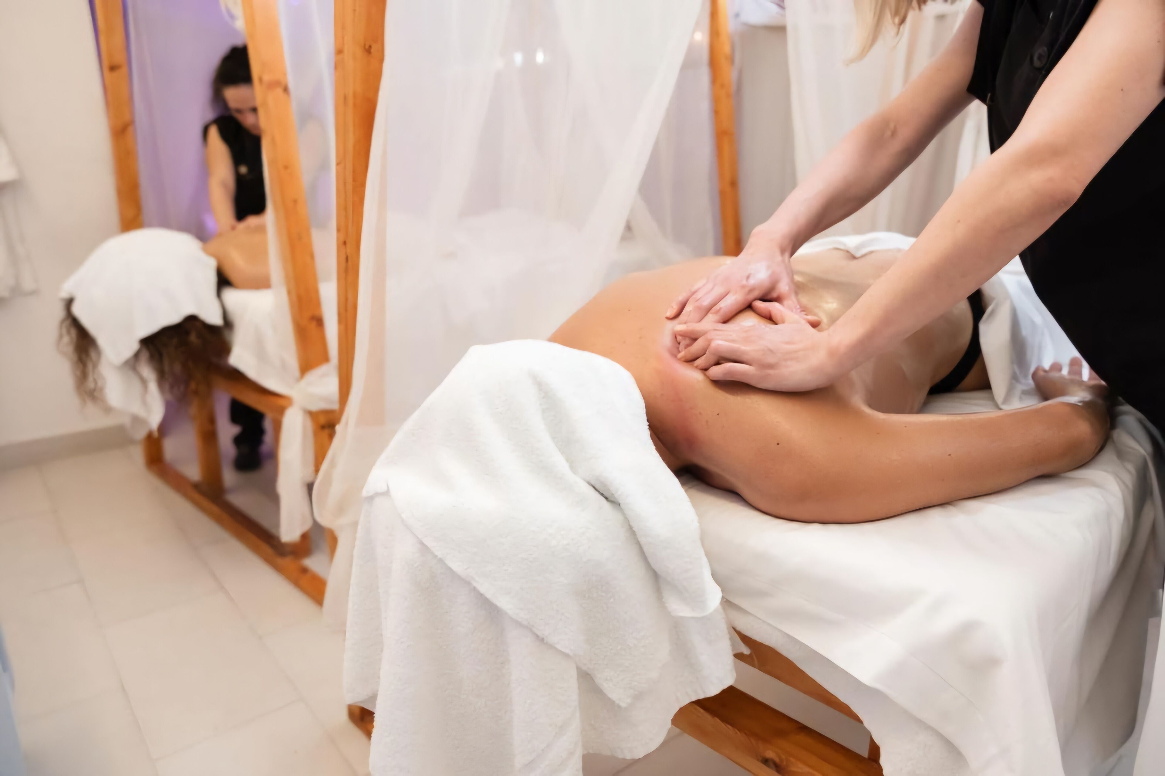 A massage therapy session in a room with wooden furniture and a white canopy.