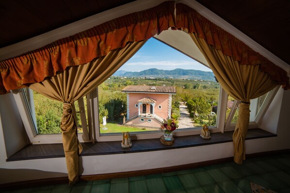 Una habitación con vistas a un paisaje rural, una ventana con cortinas y una pequeña estatua en el alféizar.