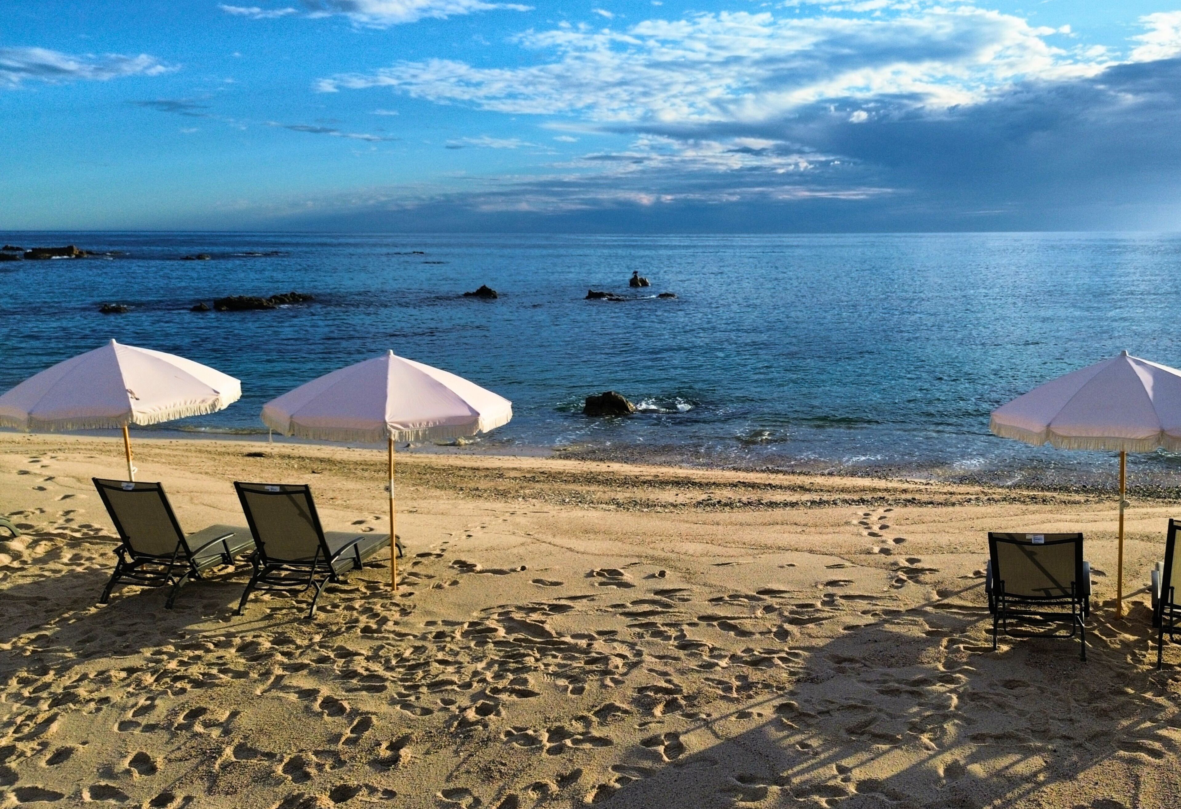 Una playa con tres sombrillas blancas y cuatro sillas de playa.