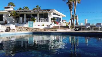 Zona de piscina con vista despejada, sillas de descanso y un edificio de fachada blanca con palmeras.