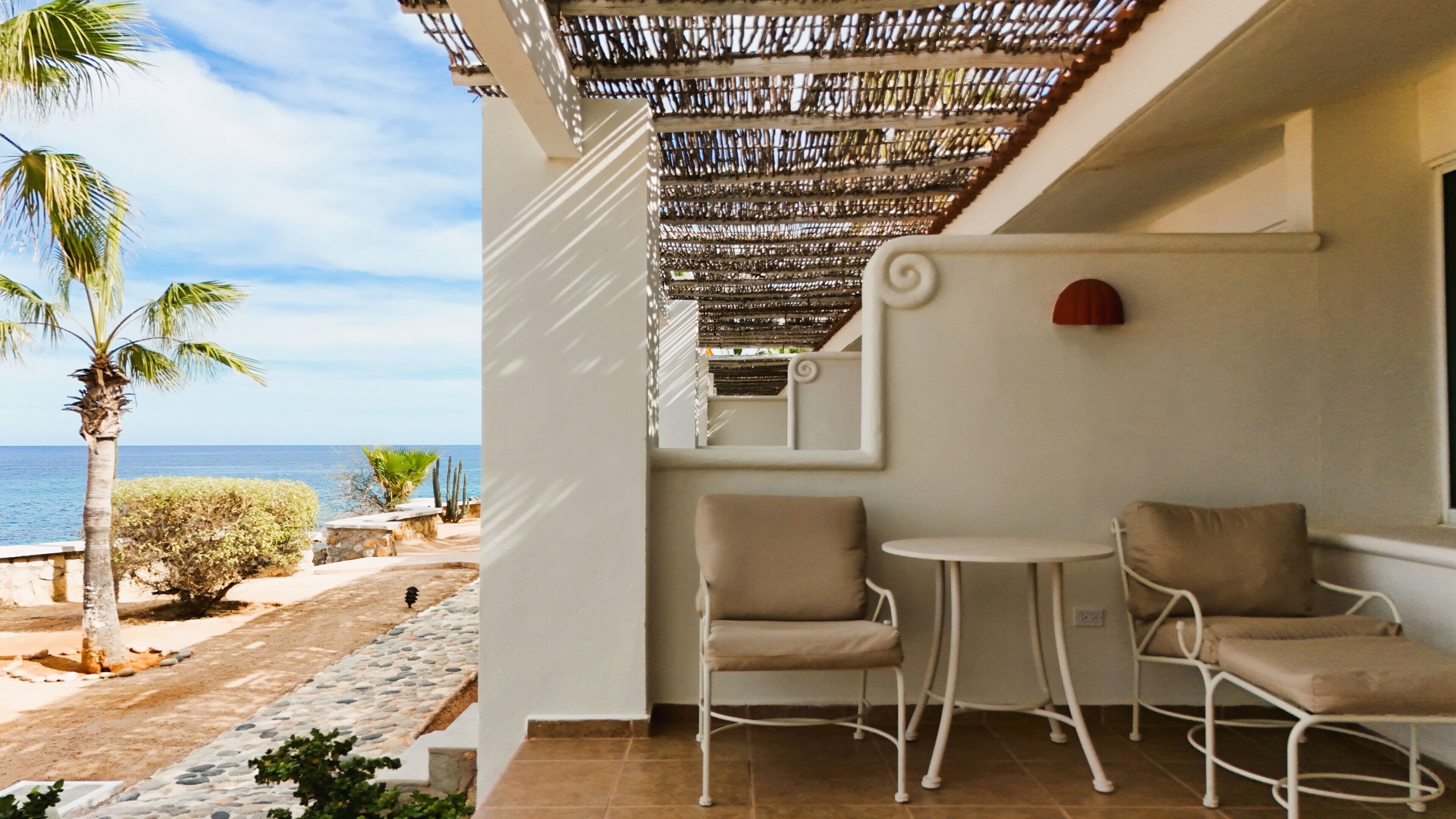Une terrasse avec deux chaises et une table, donnant sur une plage bordée de palmiers et sur la mer.