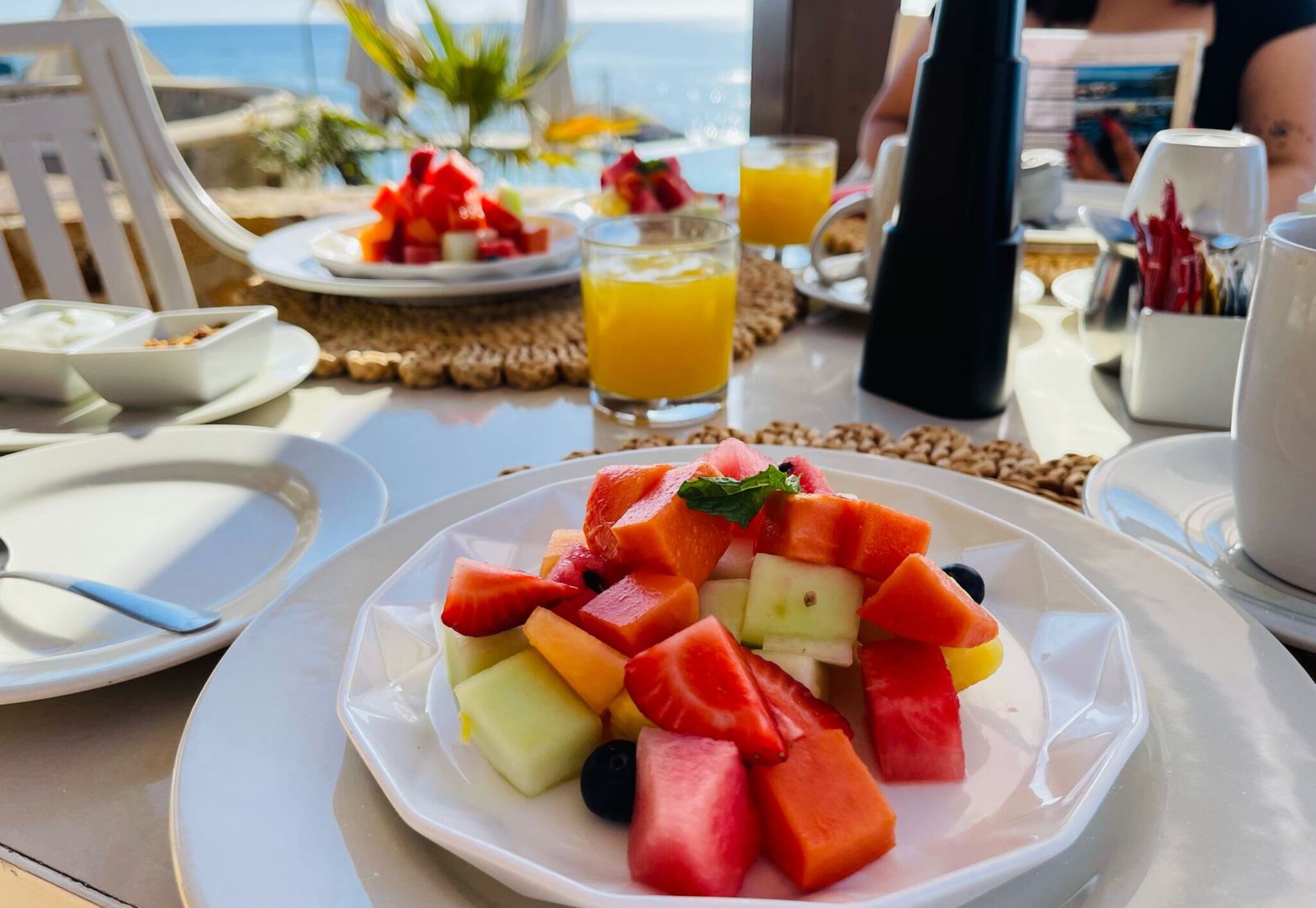 A table with a fruit salad, a glass of orange juice, and a white plate with a fork.