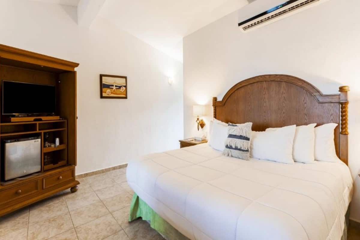 A hotel room with a large bed, a wooden TV stand, and a wall-mounted air conditioner.