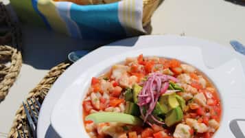 A white plate with a seafood dish, possibly ceviche, garnished with avocado and red onions, accompanied by a basket of bread and a blue napkin.