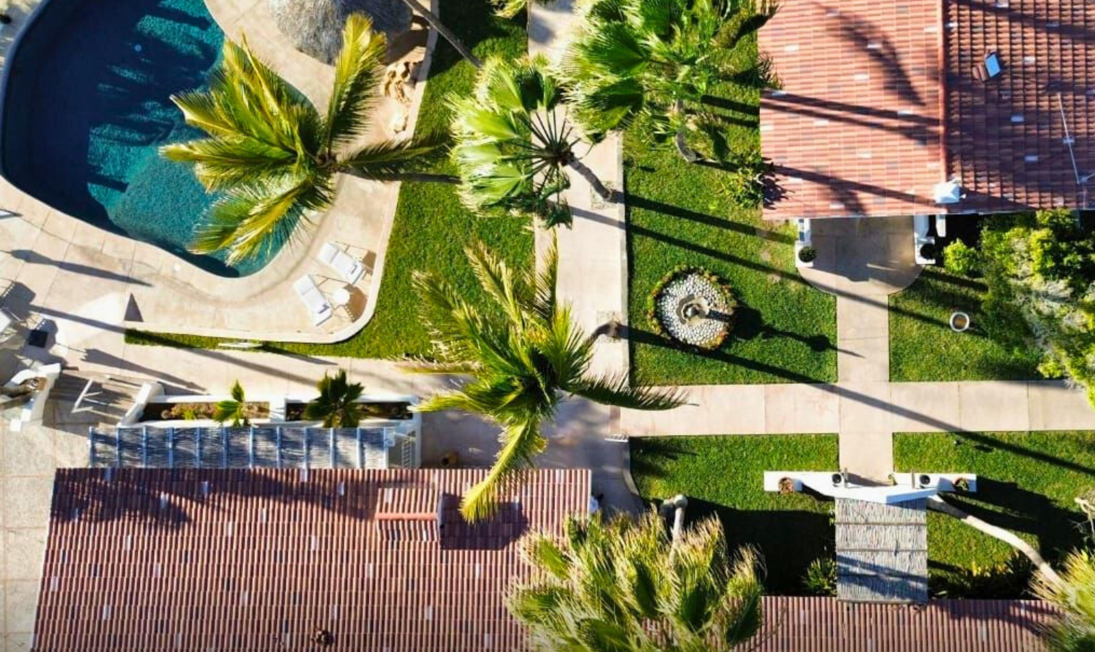 Vista aérea de un resort con piscina, palmeras y un patio con baldosas.