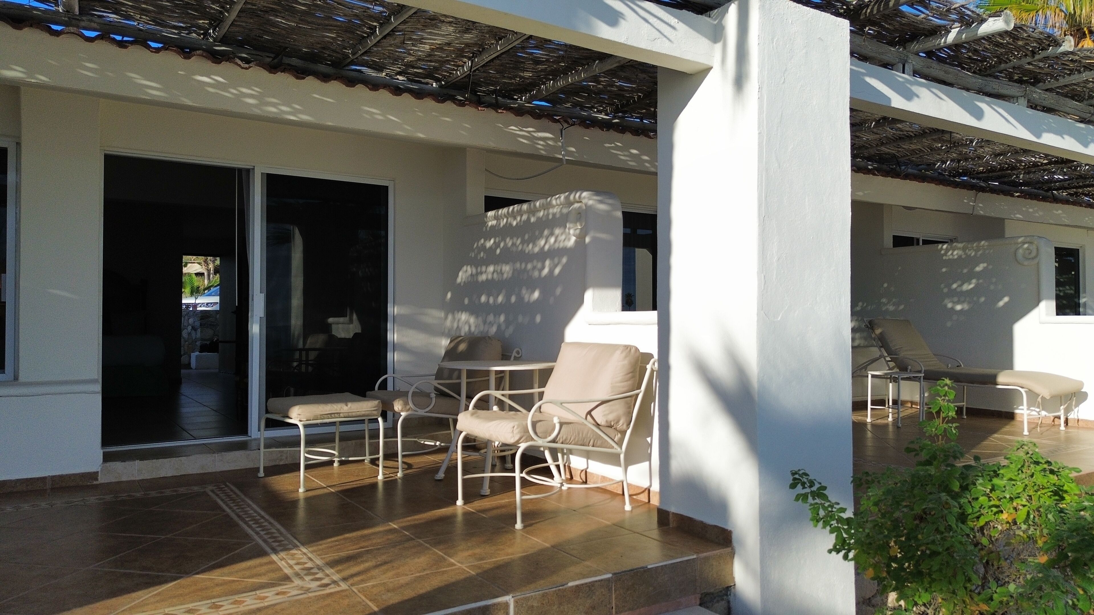 A covered outdoor seating area with chairs and a table, a sliding glass door leading to a patio, and a tiled floor.