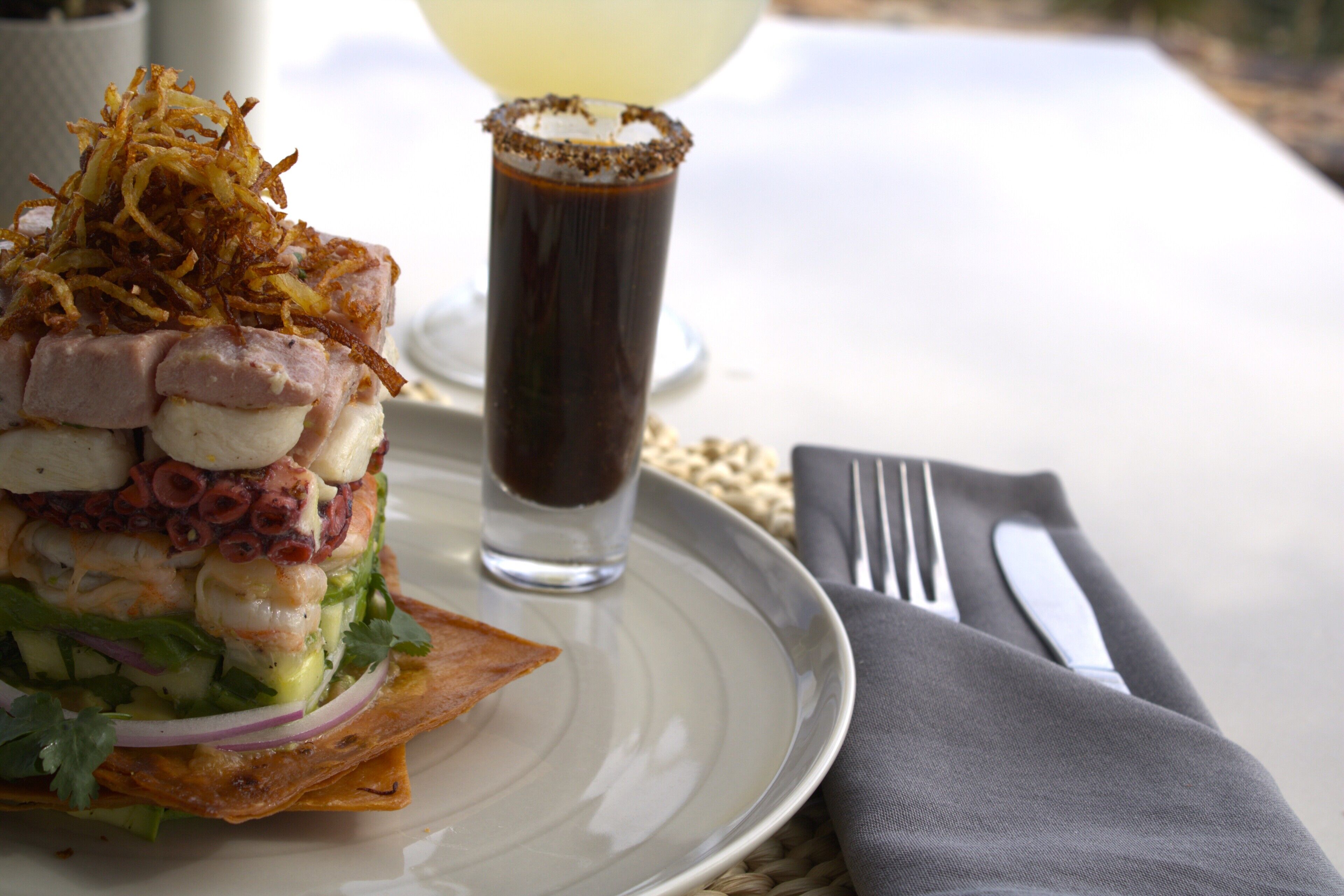 Une assiette contenant un plat de fruits de mer, un verre d’une boisson sombre, ainsi qu’une fourchette et un couteau, le tout posé sur une table.