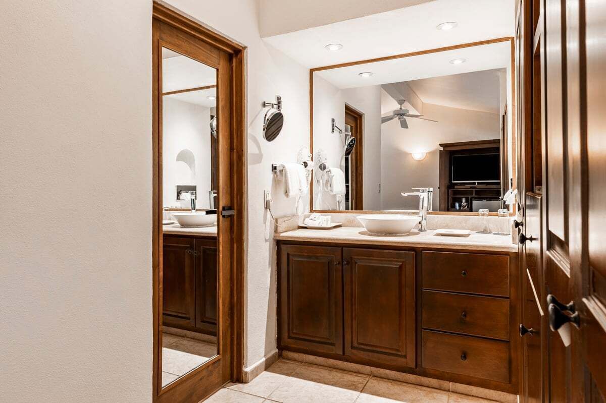 A bathroom with a large mirror, wooden cabinets, and a sink.