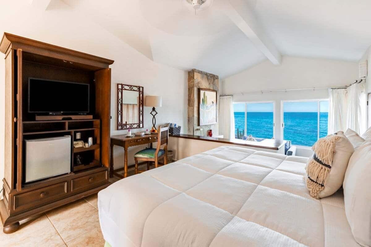 A hotel room with a large bed, a television, a desk, and a view of the ocean.