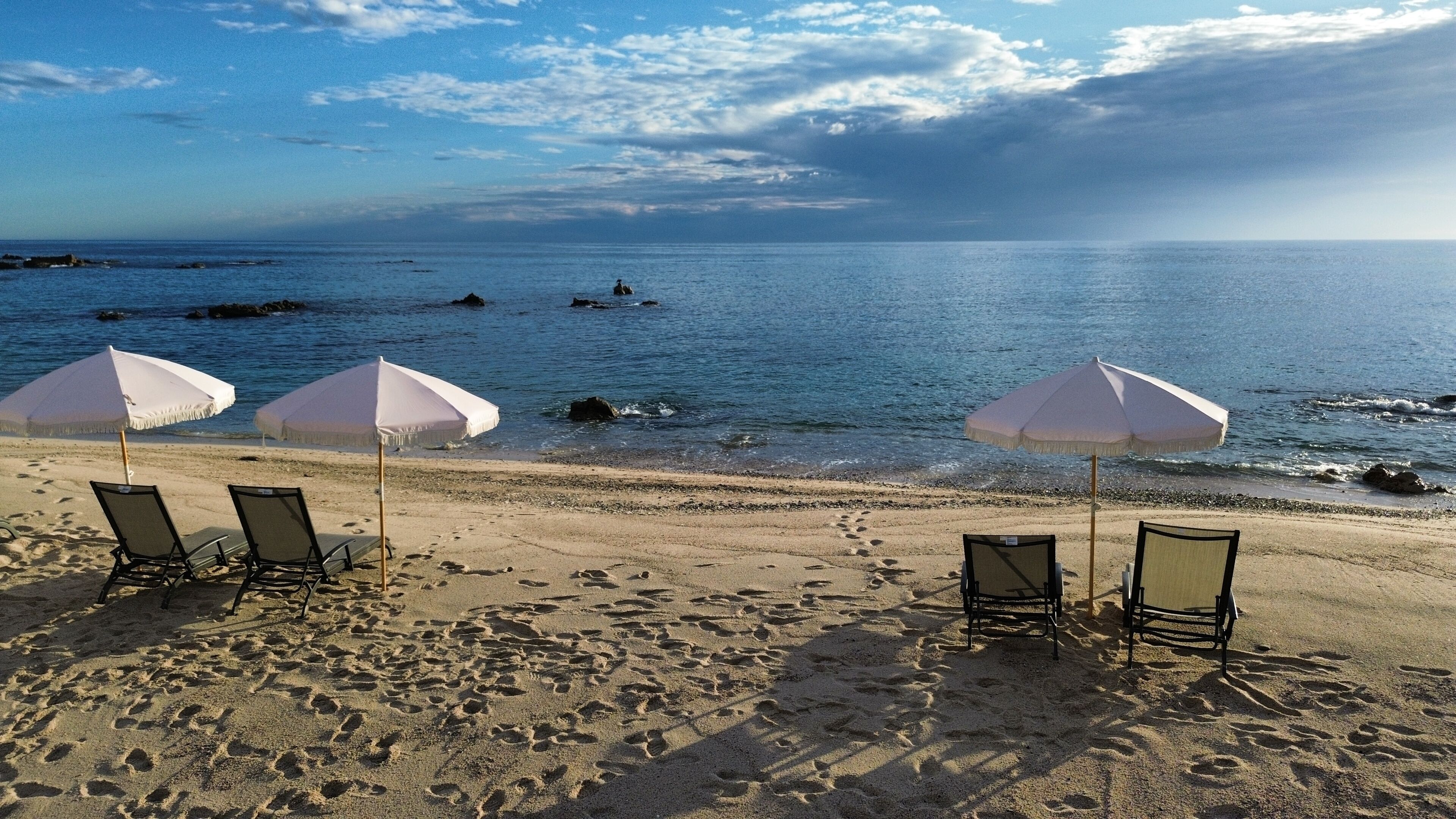 Une plage avec trois parasols blancs et quatre chaises de plage.