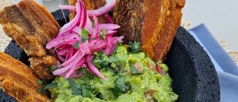 A bowl of guacamole with red onions and cilantro, accompanied by fried plantains.