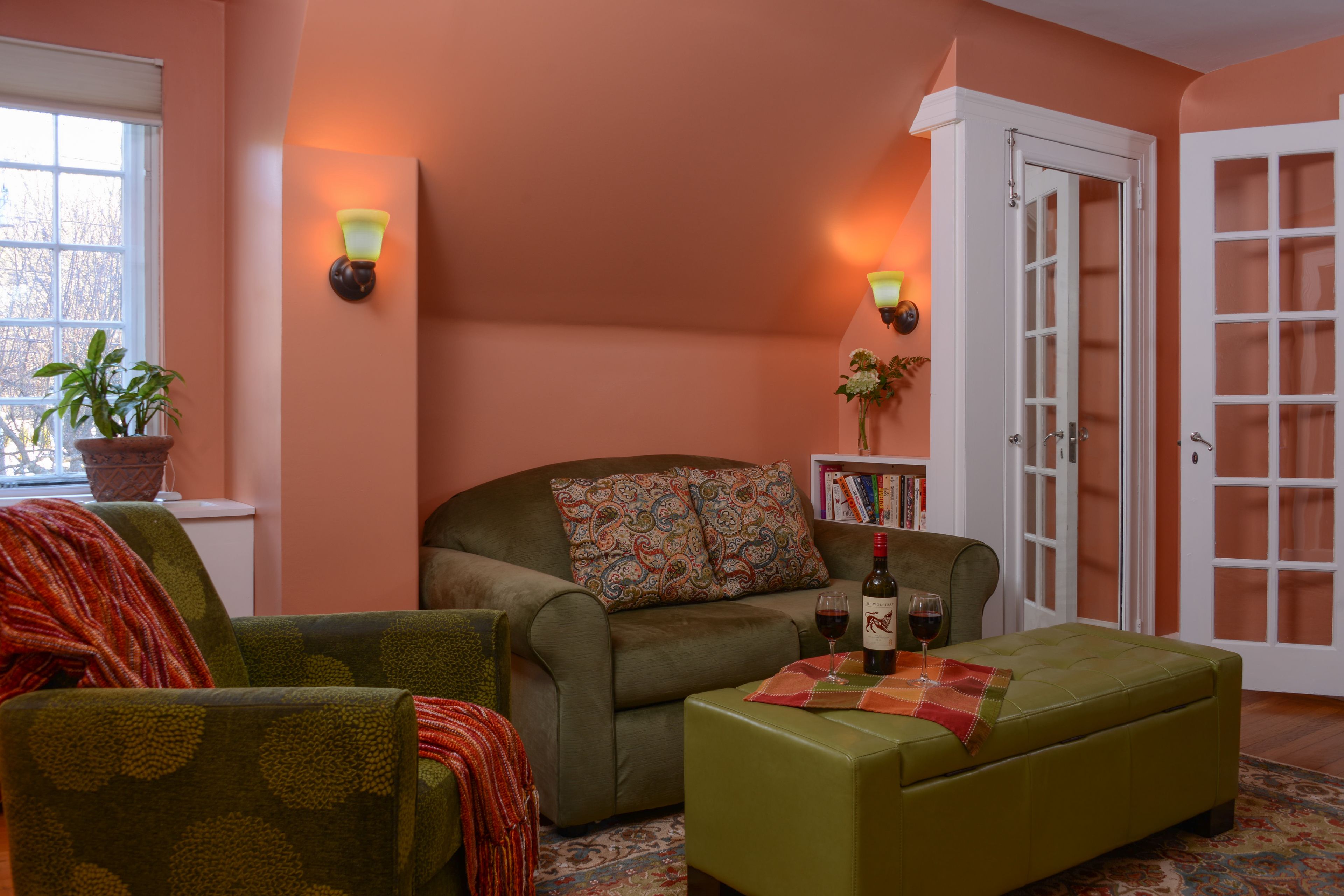 A cozy living room with a sofa, ottoman, and chairs, a bookshelf, and a door with glass panels.