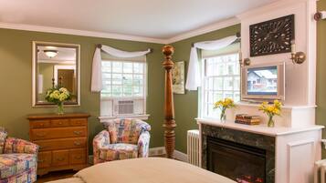 A bedroom with a bed, dresser, chair, fireplace, and a large mirror.
