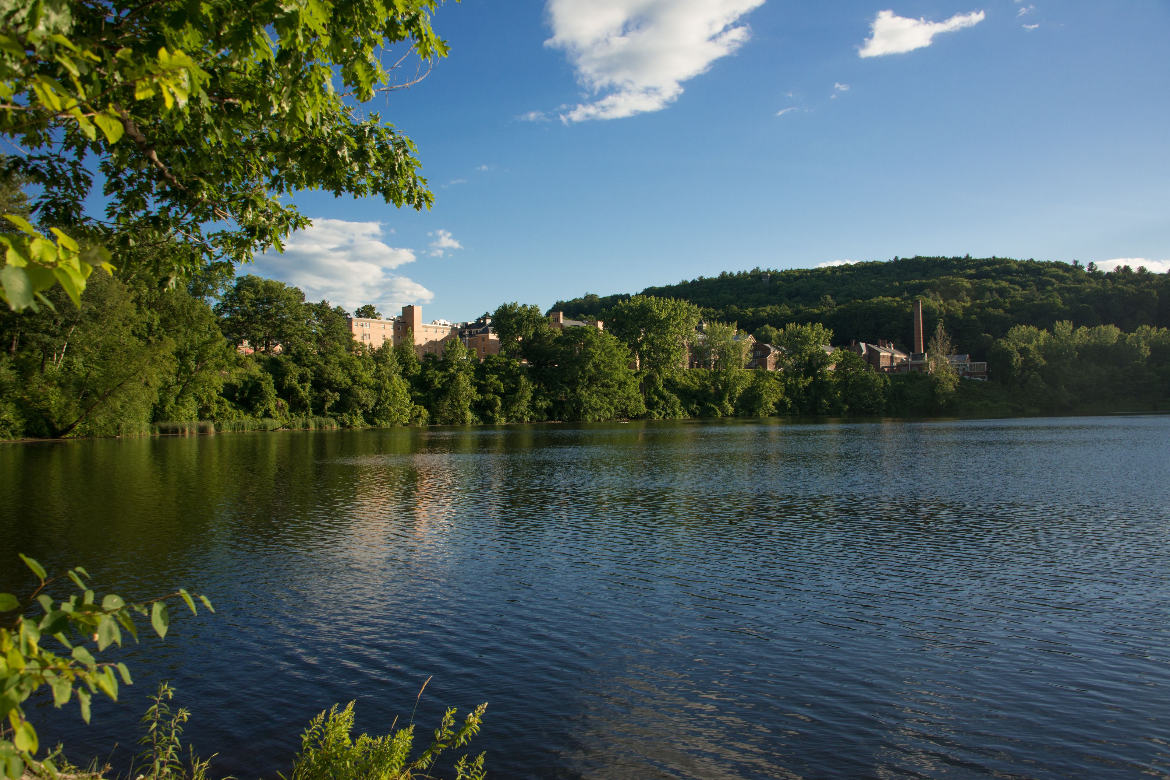 A calm lake with buildings on a hill in the background.