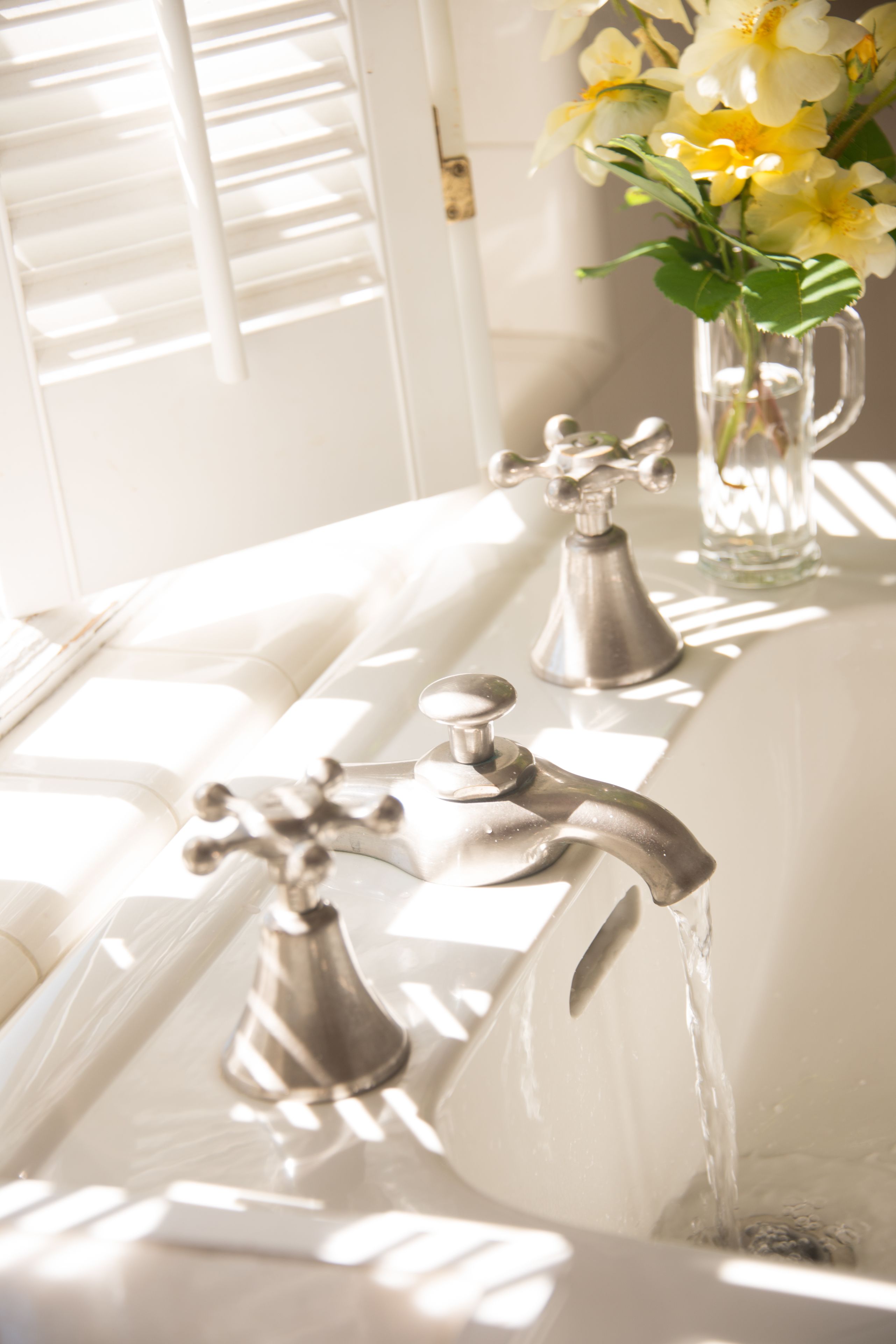 A bathroom with a white sink, two faucets, and a vase with flowers.