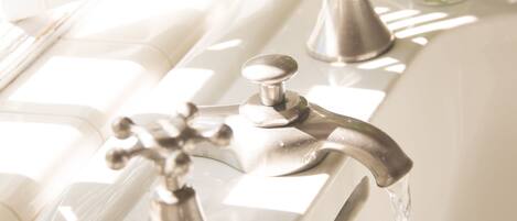 A bathroom with a white sink, two faucets, and a vase with flowers.