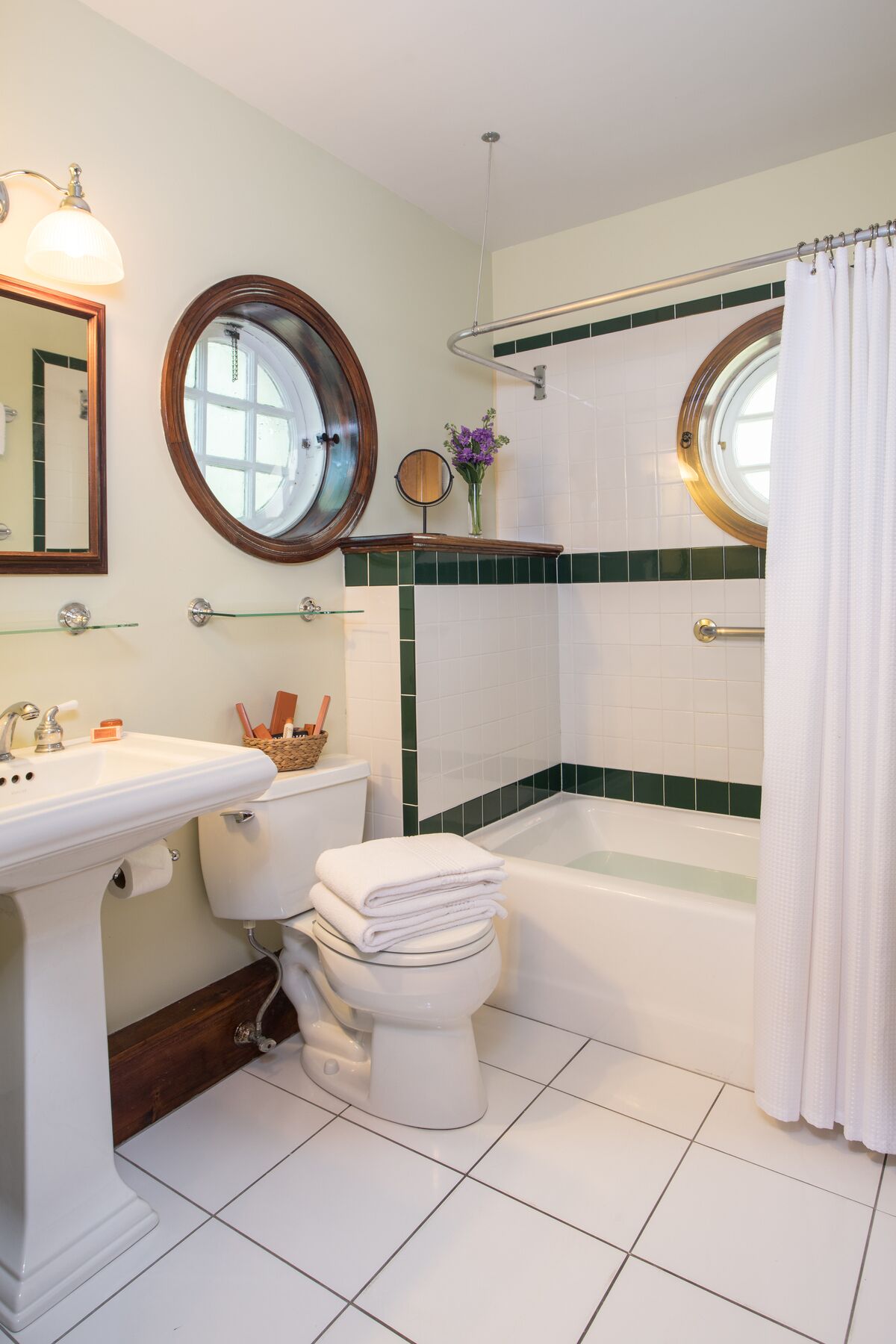 A bathroom with a white sink, toilet, and bathtub, a round mirror, and a shower curtain.