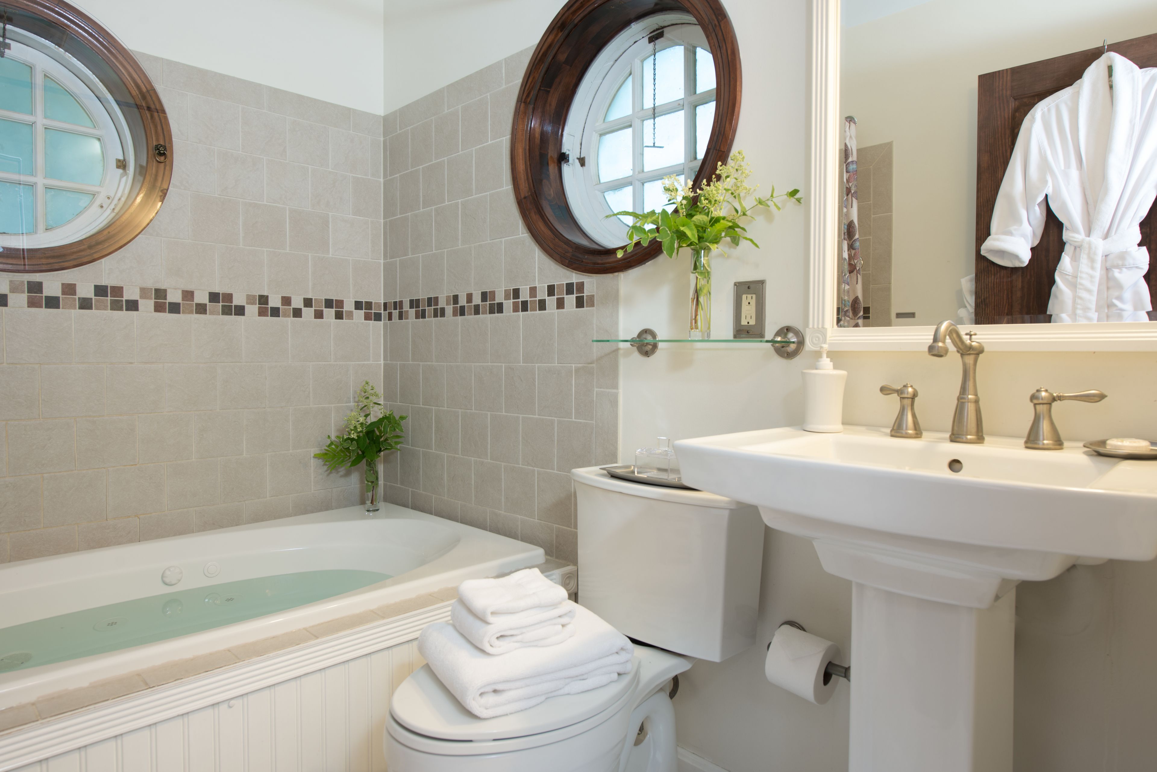 A bathroom with a bathtub, toilet, sink, and a mirror with a robe hanging.