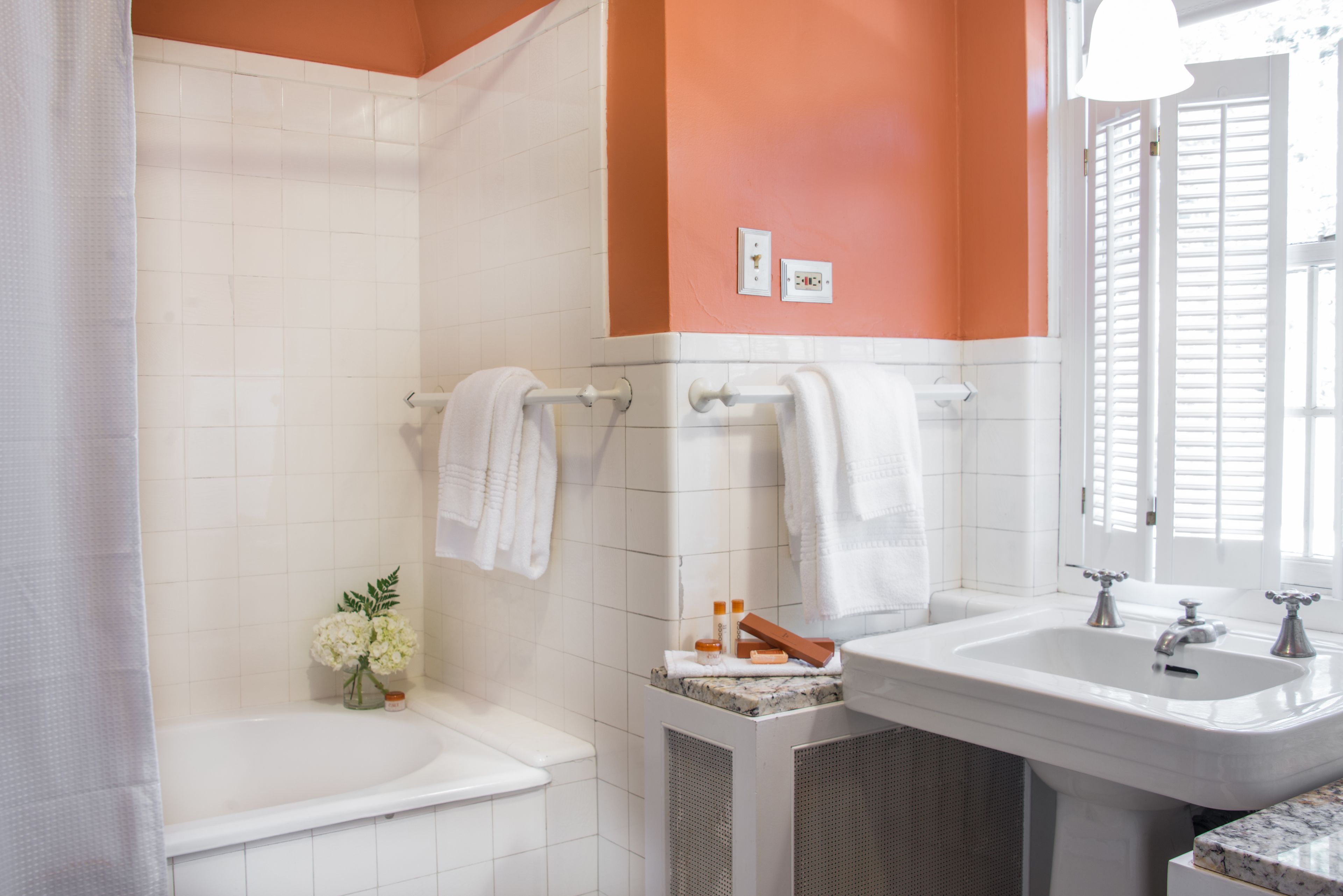 A bathroom with a bathtub, a sink, and a shower. There are towels hanging on a rack, a small vase with flowers, and toiletries on the sink.