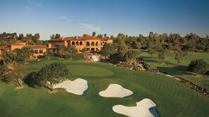 A golf course with sand bunkers, a large building with arches, and surrounding trees.