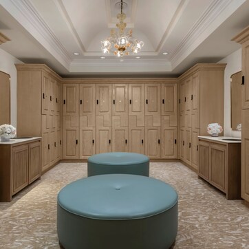 A spacious room with wooden cabinets, a chandelier, and two round ottomans.