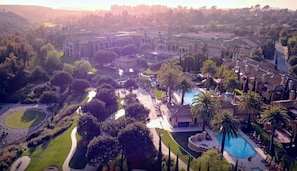 An aerial view of a resort with a swimming pool, palm trees, and a large building complex.