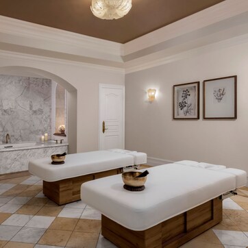 A spa area with two treatment beds, a marble wall, a sink, and framed botanical artwork.