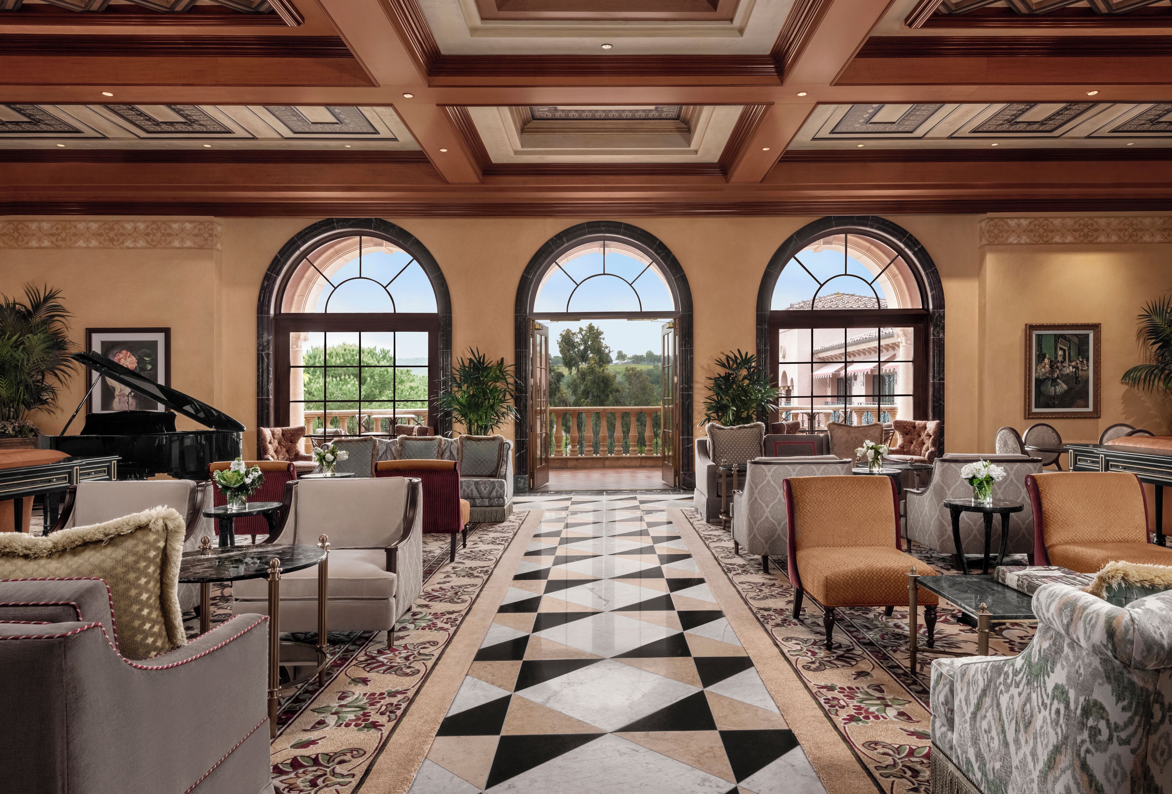A spacious lobby with a checkered floor, multiple seating areas, and large arched windows offering a view of the outdoors.