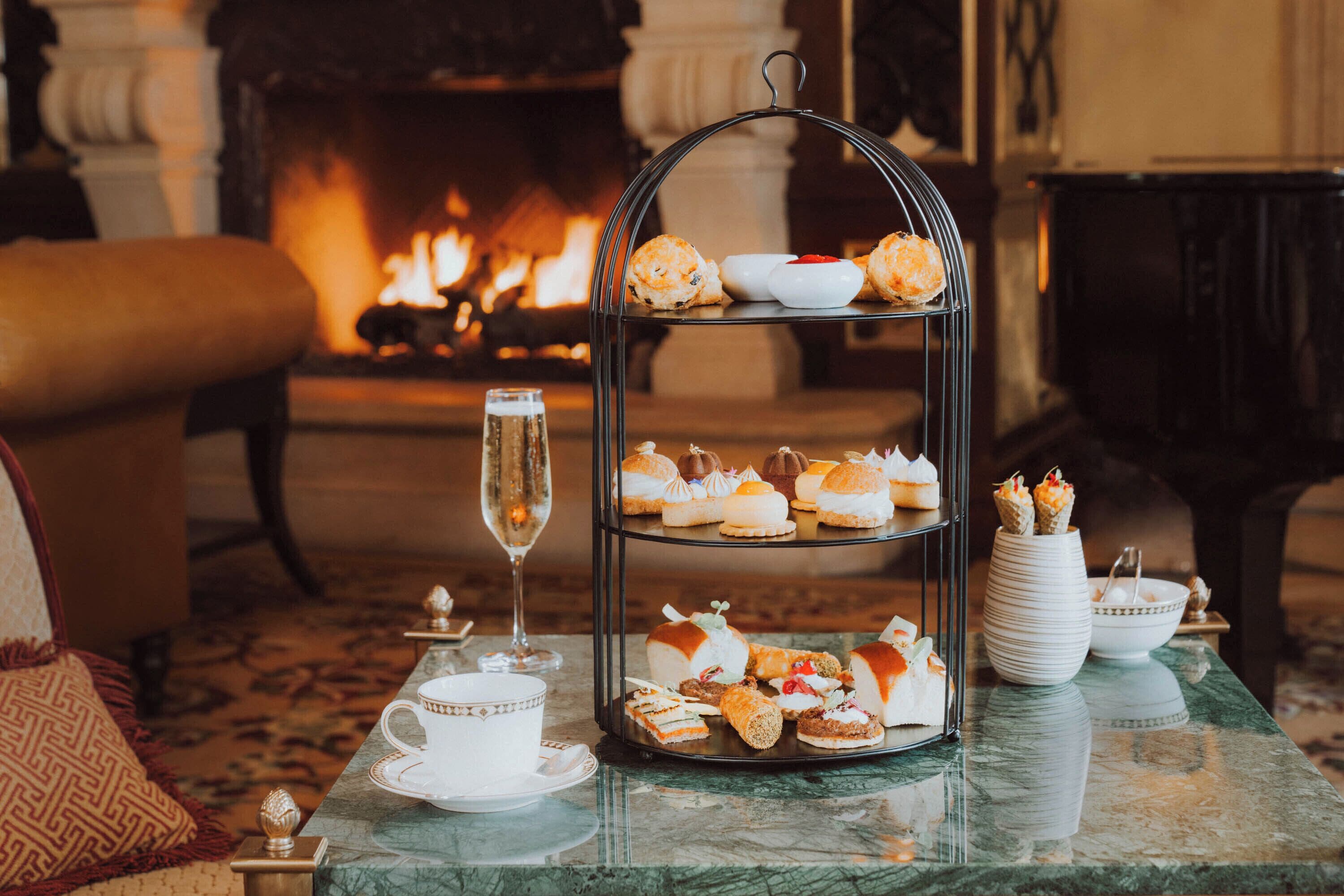 A three-tiered dessert display on a table with a fireplace in the background.