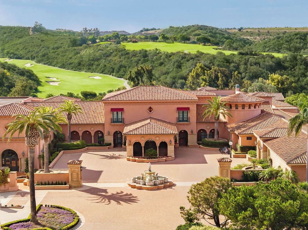 A Mediterranean-style building with a courtyard, palm trees, and a golf course in the background.