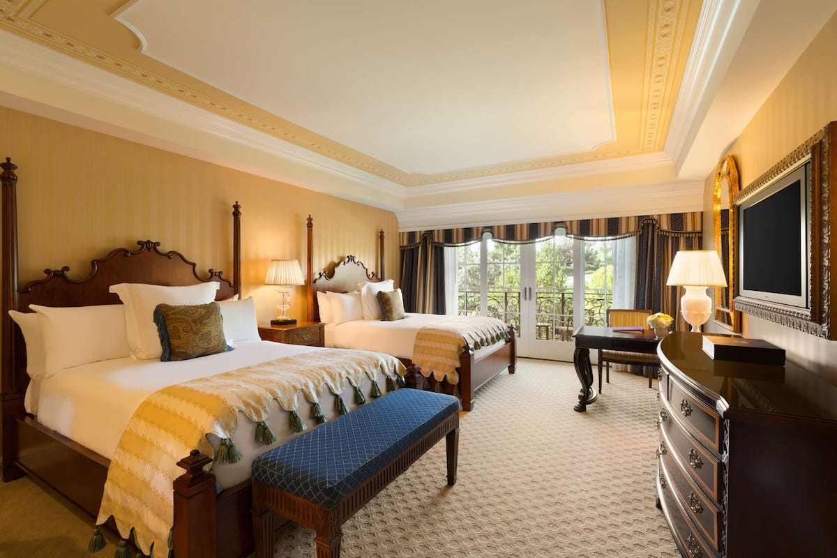 A hotel room with two beds, a bench, a dresser, and a television.