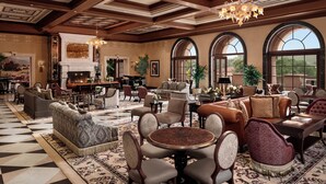 A spacious lobby with a checkered floor, multiple seating areas, a grand piano, and large arched windows.