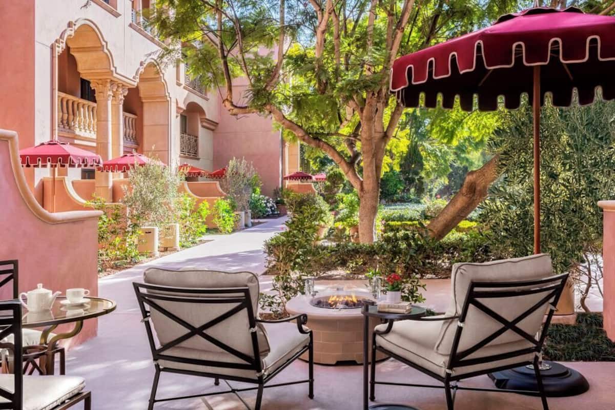 An outdoor seating area with two chairs and a table, a fire pit, and red umbrellas.