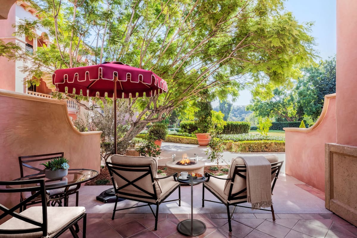 An outdoor patio with a round table, two chairs, a red umbrella, and a fire pit.