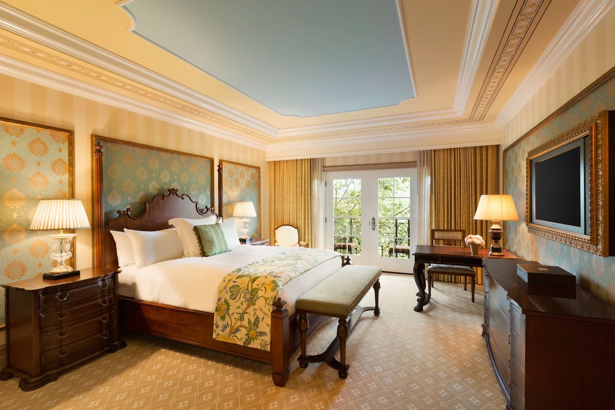 A hotel room with a large bed, a bench, a dresser, a desk, and a television.