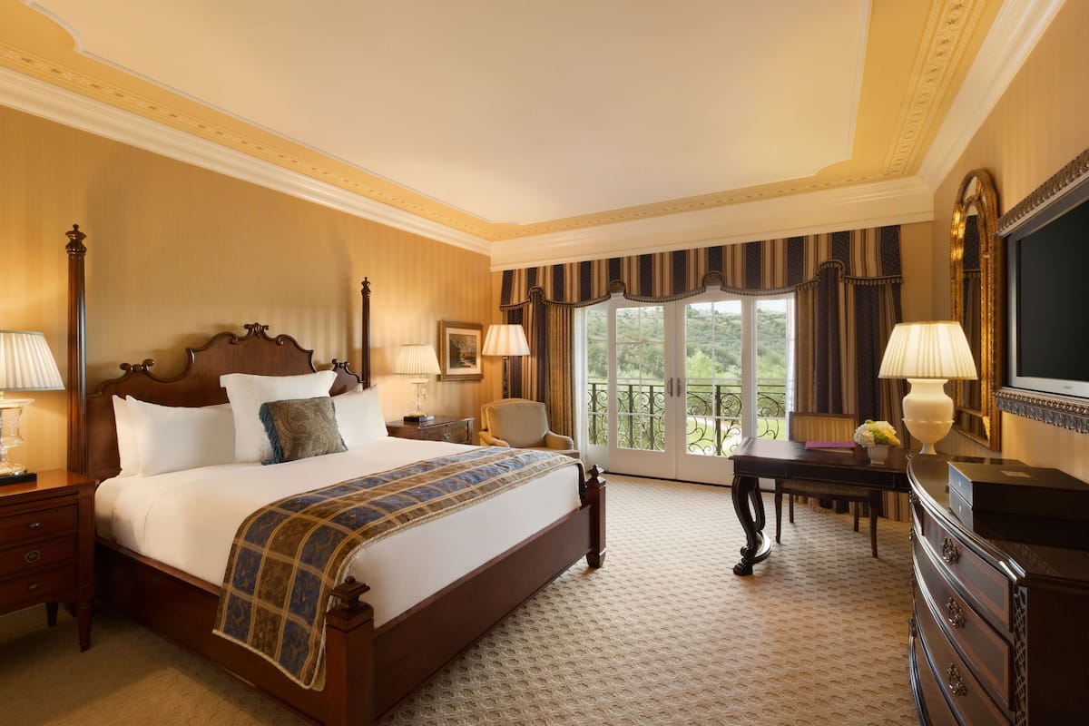 A spacious hotel room with a large bed, a desk, and a balcony with a view.