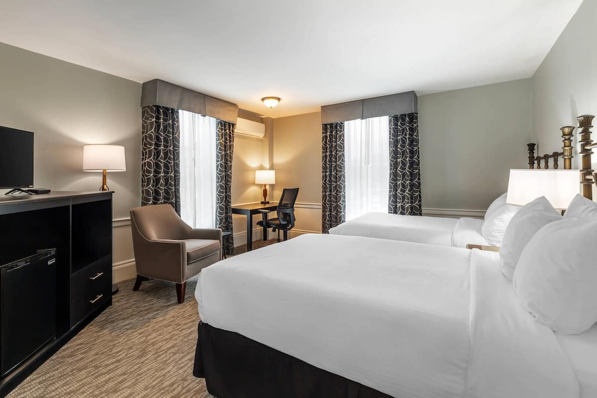 A hotel room with two beds, a desk, a chair, a TV, and a minibar.