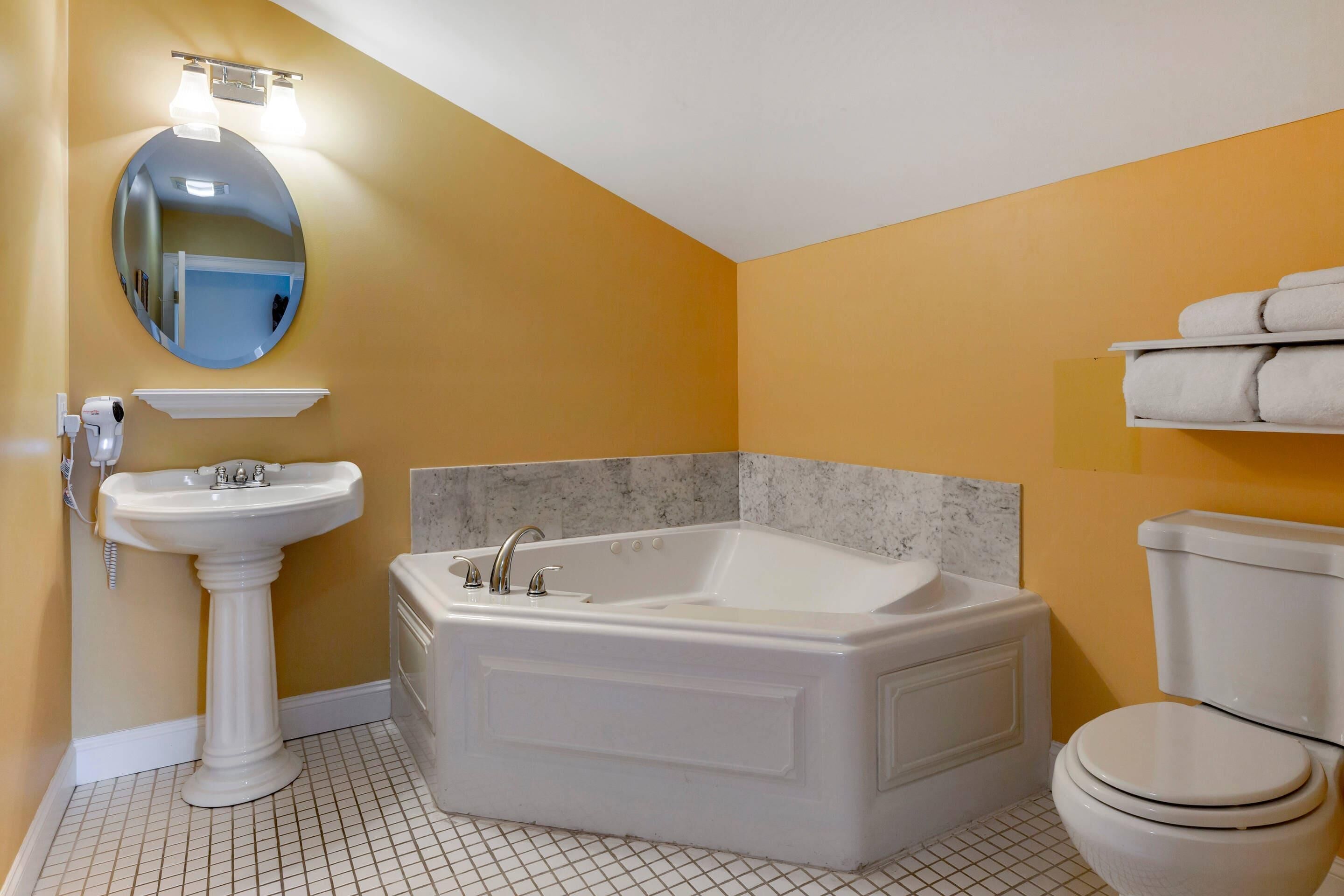 A bathroom with a pedestal sink, a freestanding bathtub, a toilet, and a mirror with lights.