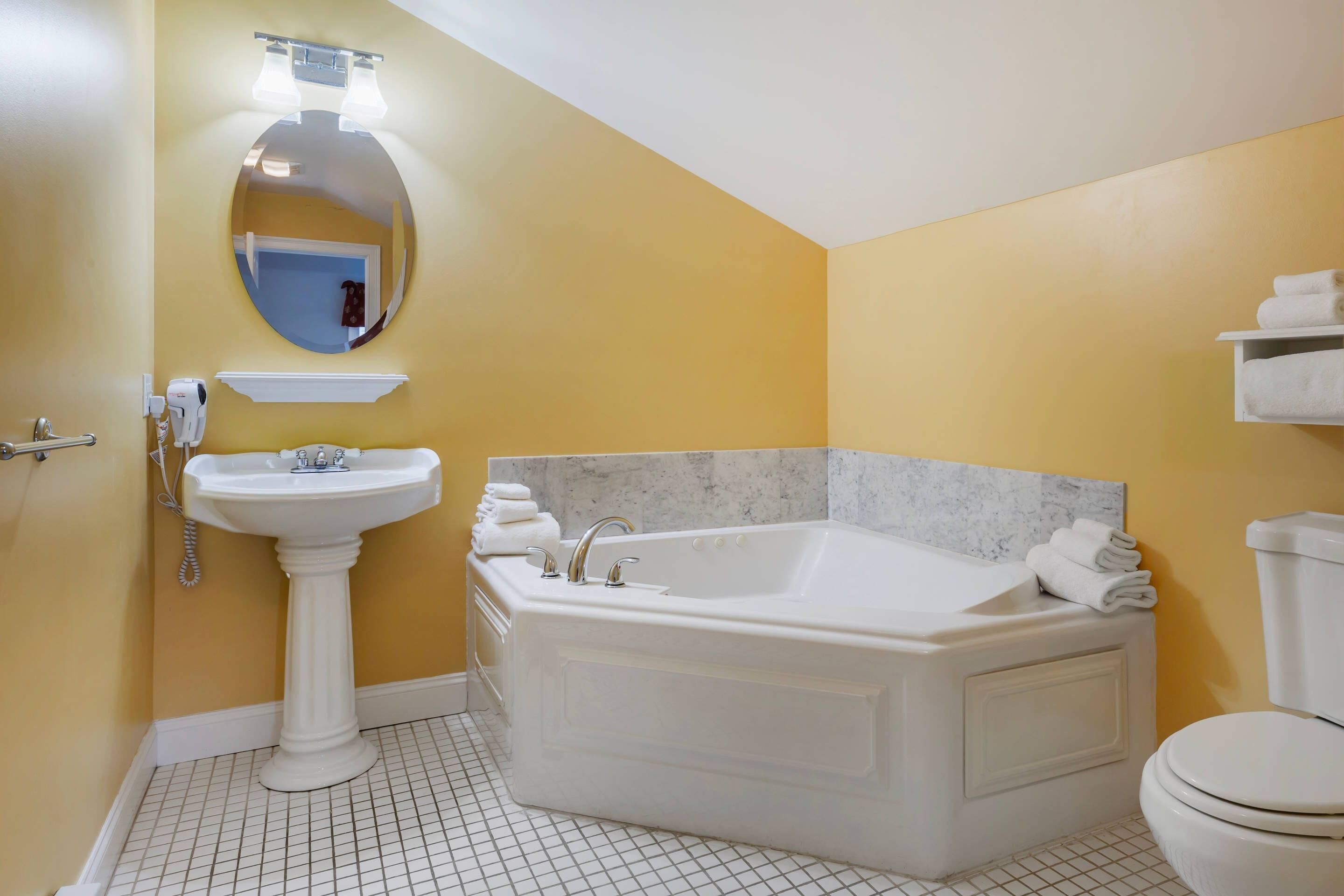 A bathroom with a pedestal sink, a freestanding bathtub, a toilet, and a mirror with lights.