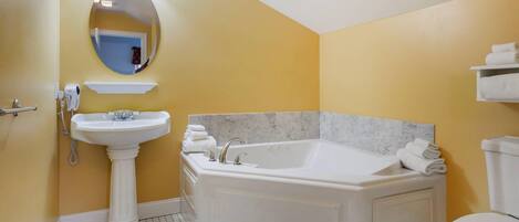 A bathroom with a pedestal sink, a freestanding bathtub, a toilet, and a mirror with lights.