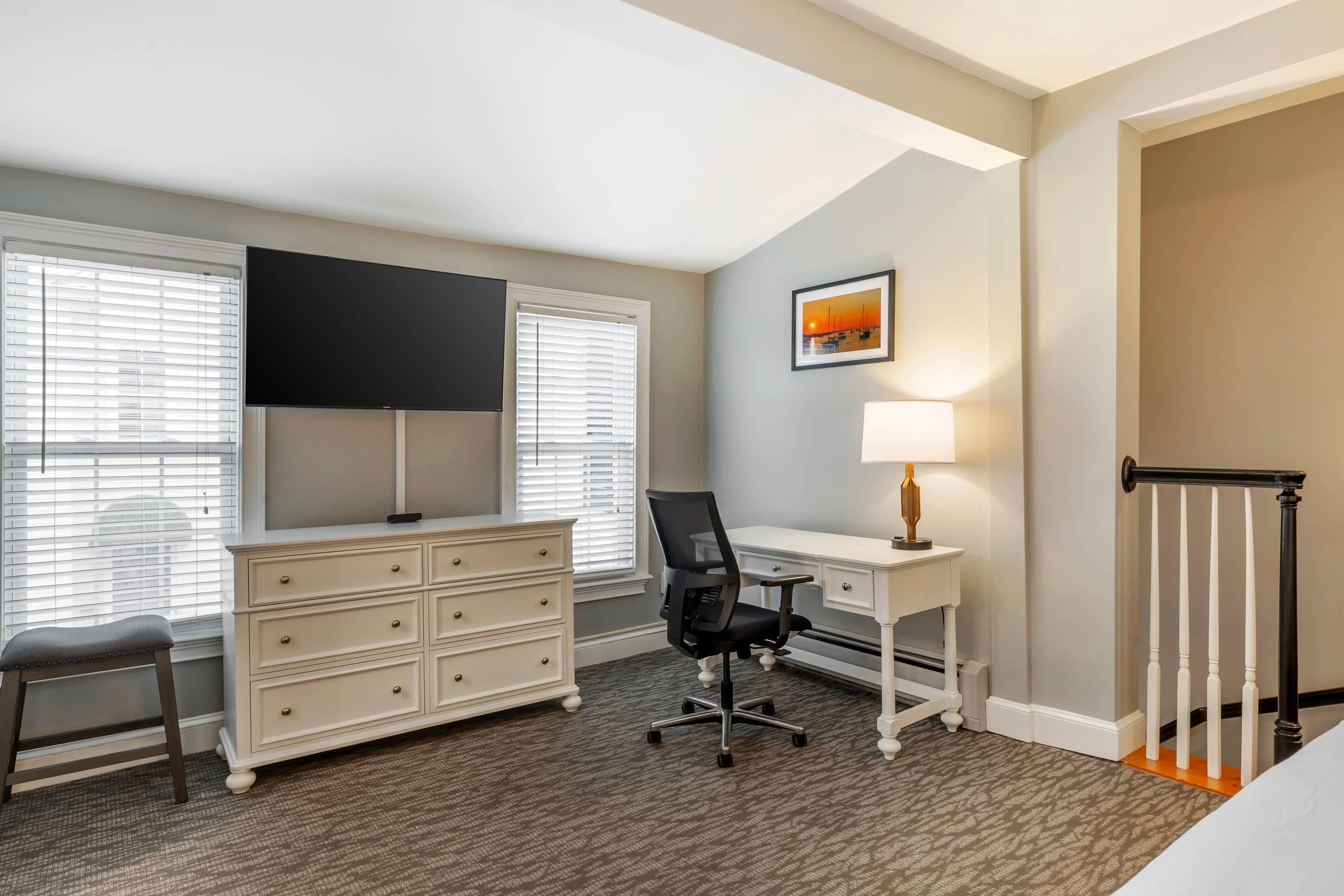 Une chambre d’h ôtel équipée d’un bureau, d’une chaise, d’une commode et d’un téléviseur fixé au mur.