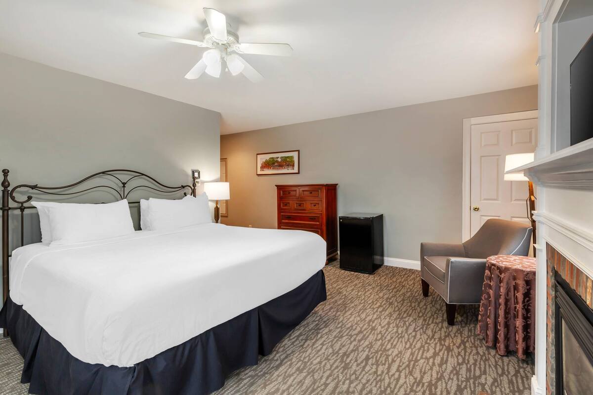 A hotel room with a large bed, a ceiling fan, a dresser, a chair, and a small table.