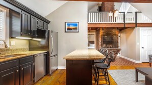 A kitchen with dark cabinets, a granite countertop, and a central island with chairs. - Essex Street Inn & Suites, an Ascend Collection Hotel (Newburyport)