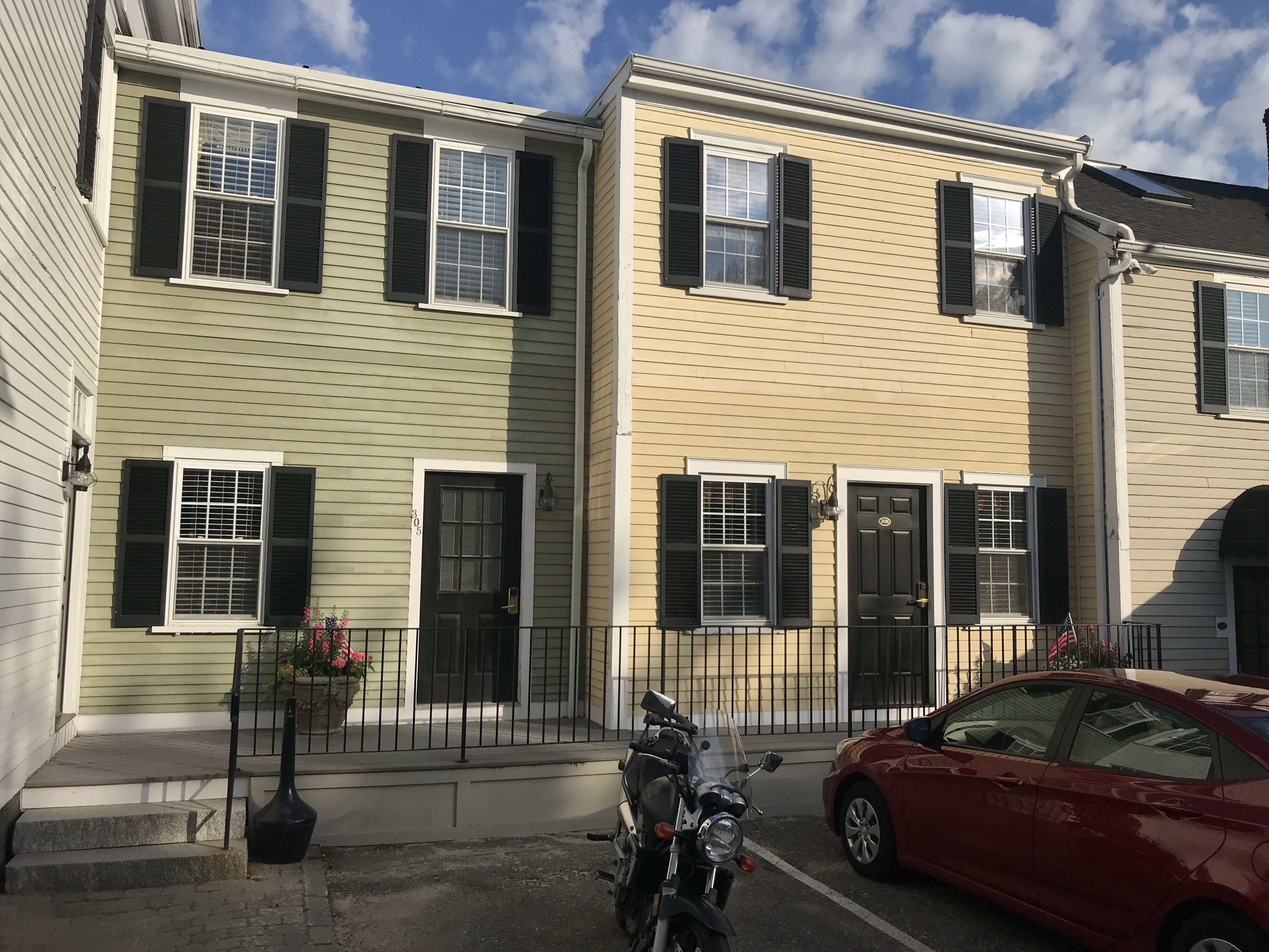 A row of townhouses with a motorcycle parked in front and a red car parked on the street.