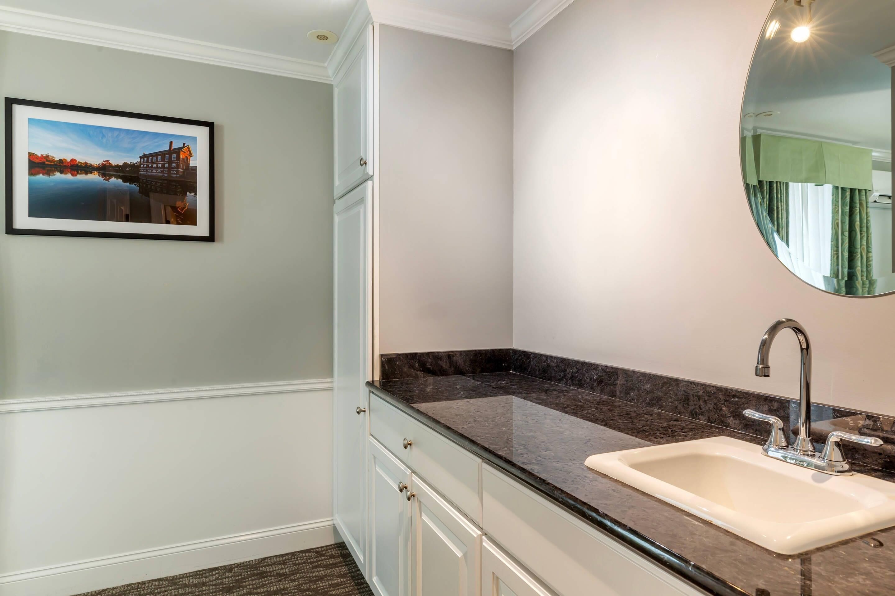 Un baño con encimera de mármol, un lavabo con grifo moderno, un cuadro en la pared y un espejo grande.