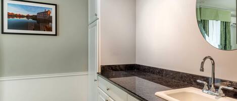 Un baño con encimera de mármol, un lavabo con grifo moderno, un cuadro en la pared y un espejo grande.