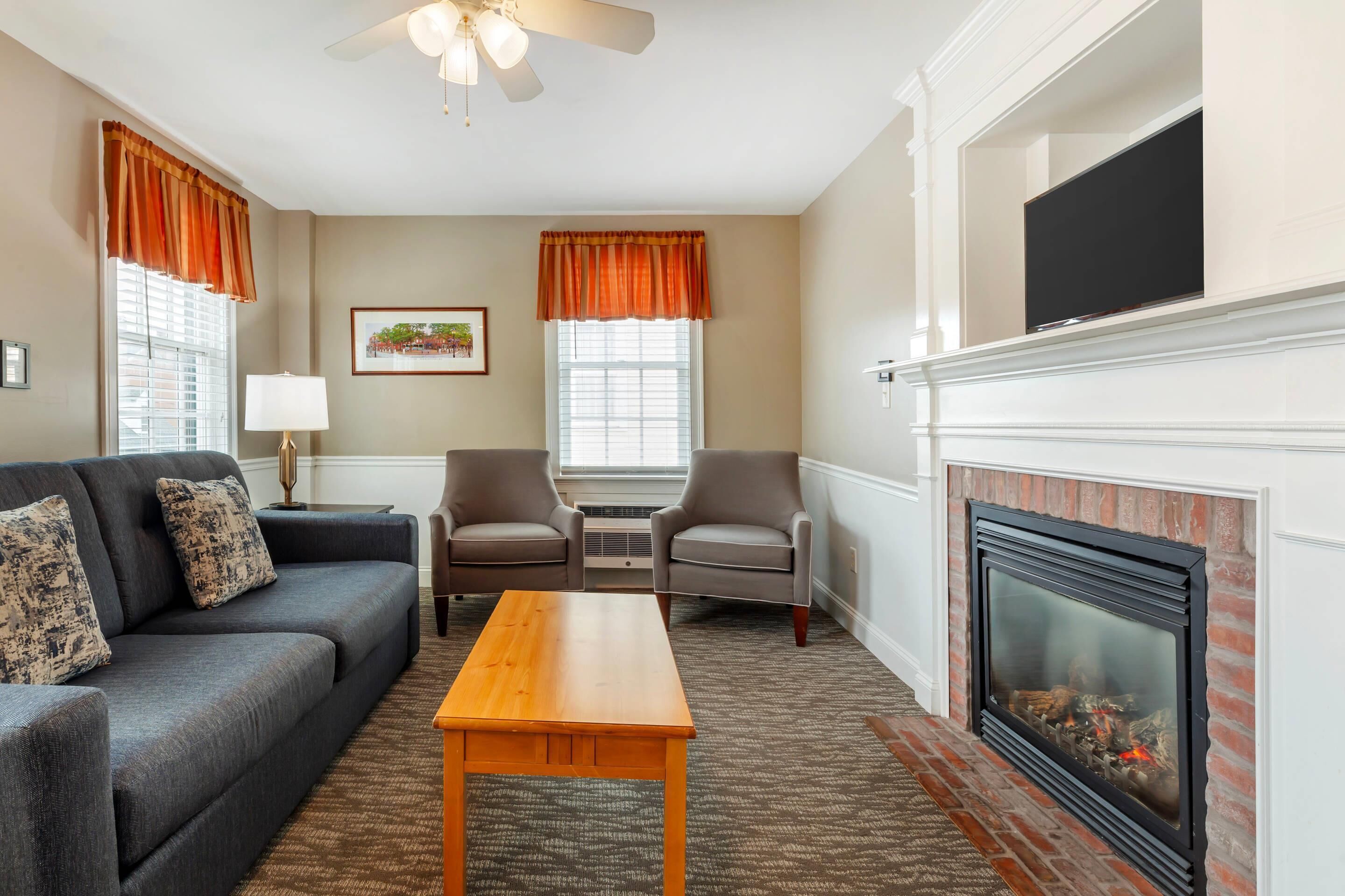A living room with a sofa, two armchairs, a wooden coffee table, a fireplace, and a ceiling fan.
