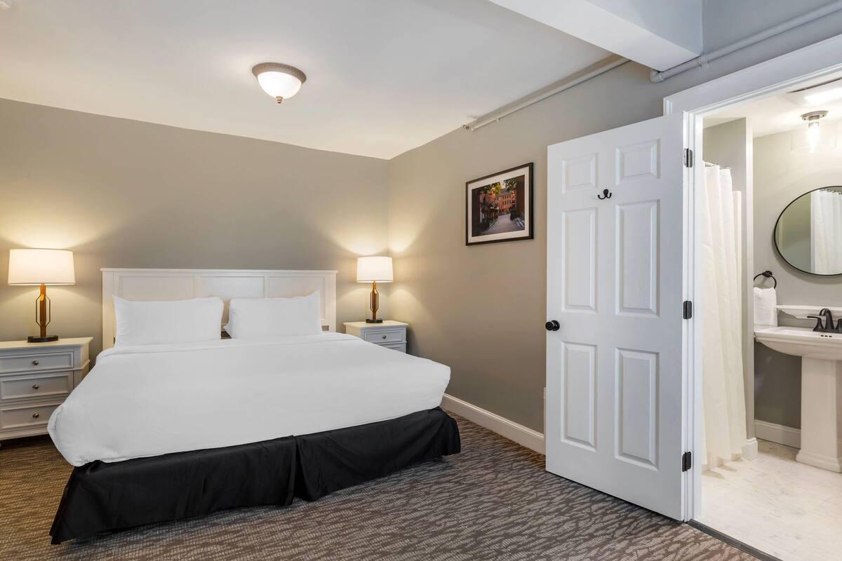 A hotel room with a large bed, bedside lamps, a door leading to a bathroom, and a framed picture on the wall.