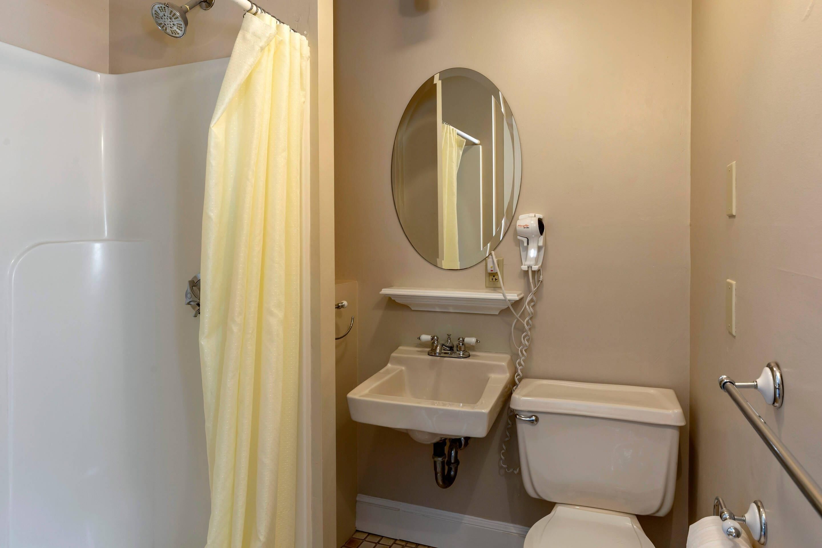 A bathroom with a shower, toilet, sink, and a mirror.