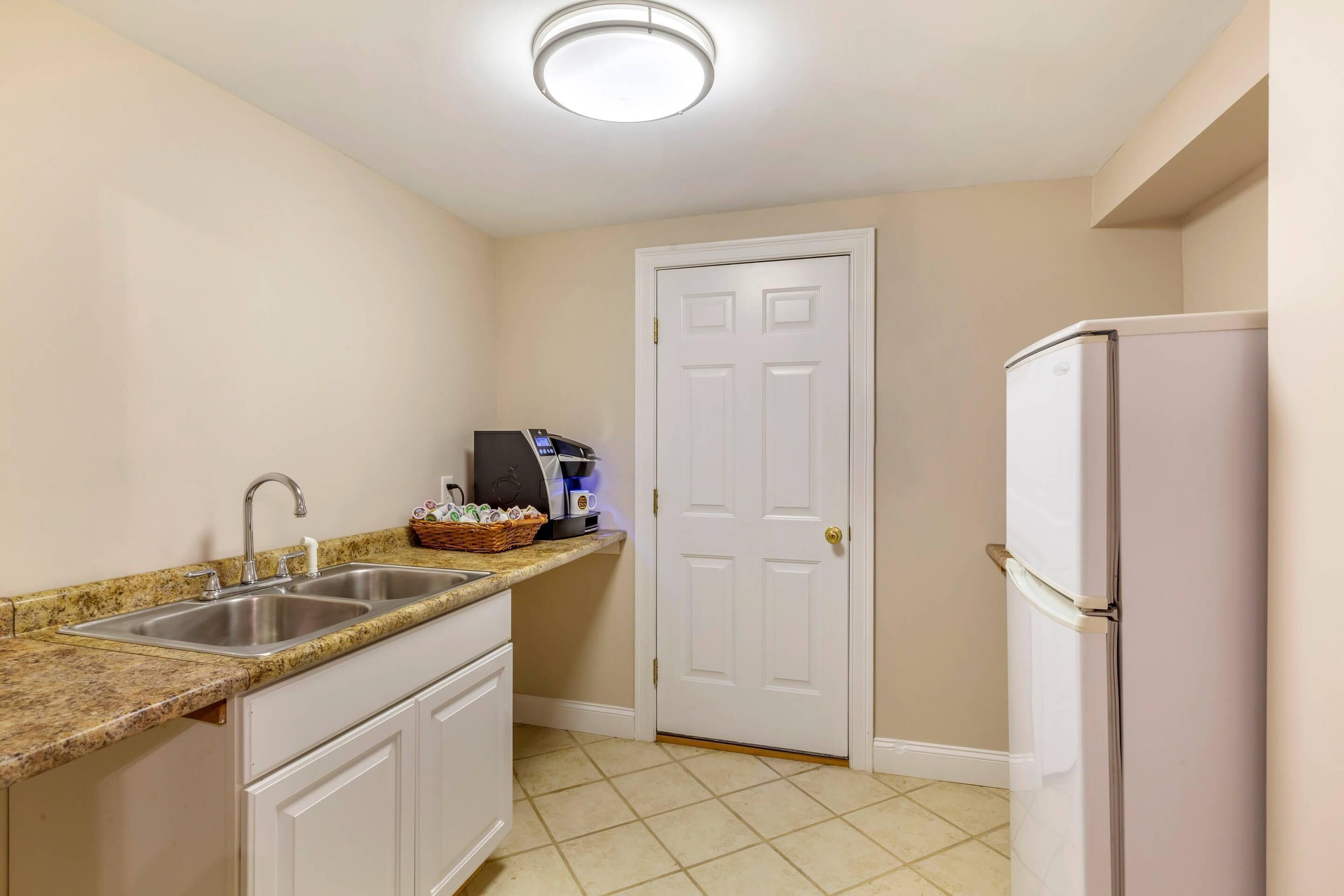 A compact kitchen with a double sink, a coffee maker, and a refrigerator.